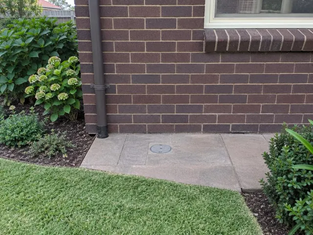 Flush capped inspection point in paved garden area beside a brick house in Haberfield